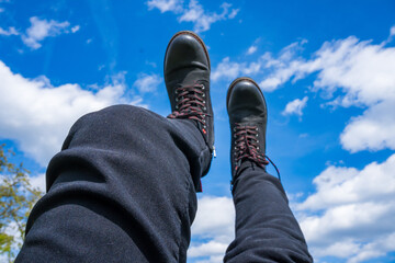 Hanging feet with mountain boots, sky in background, beautiful nature scenario
