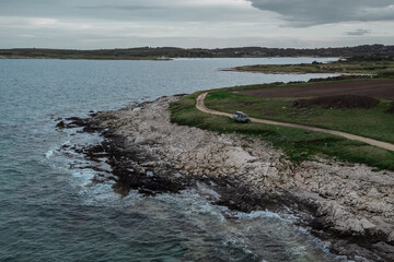 Adventure camper parked on a penninsula with rocks and wild sea. Road trip through istrian landscape. Discover istria, croatia. Gray day.
