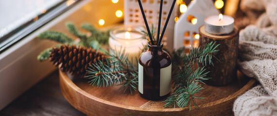 Aroma burning candles, aromatic reed diffuser in glass bottle. Cozy Christmas atmosphere at home. Holiday scent, aromatherapy. Fir tree fragrance, winter mood, decoration, knitted sweater. Banner
