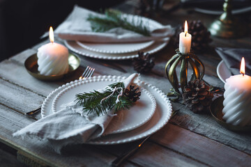 Elegant decor for Christmas family dinner. Center piece with burning candles, vintage chandelier. Zero waste eco-friendly reusable home decoration, fir tree branches. Cozy atmosphere, wooden furniture