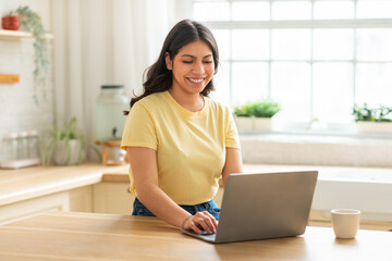 A middle eastern woman is sitting at a table, focused on her laptop computer. She appears engrossed...