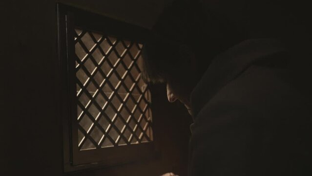 Christian woman crossing herself near confessional booth in church slow motion. Religious person praying during confession close up. Worship and faith concept