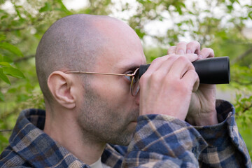 person in green bushes observes object through binoculars, espionage, covert surveillance...