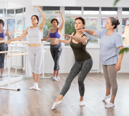 Elderly female teacher corrects the movements of novice dancers in studio