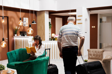 Arriving in contemporary hotel lobby is an elderly caucasian man who goes to front desk to check...