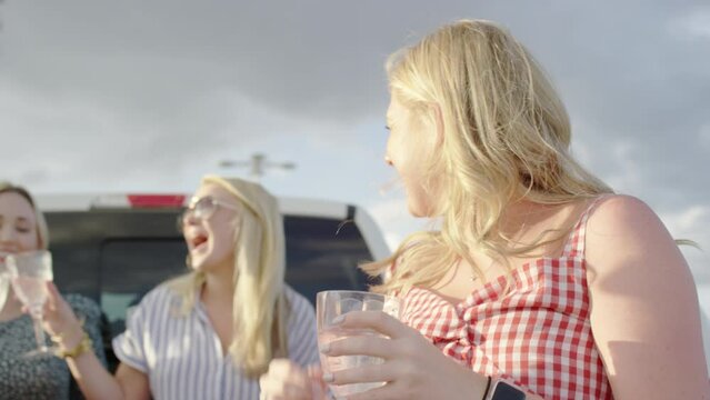 Carefree women hangout in the back of a truck at a tailgate and drink champagne