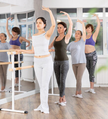 Group of female beginners practicing third ballet position at barre in dance studio