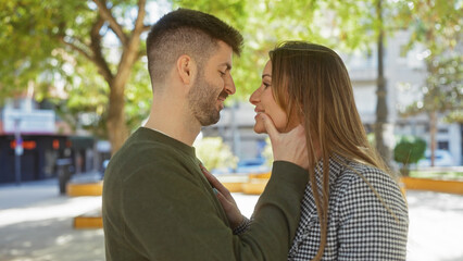 Obraz premium Romantic couple embracing outdoors in an urban park setting with affectionate gaze, showcasing love and relationship.