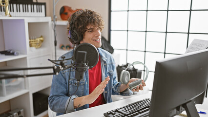 Handsome hispanic man with wavy hair smiling while recording and interacting with a microphone in a...