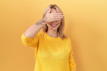 Young caucasian woman wearing yellow sweater smiling and laughing with hand on face covering eyes for surprise. blind concept.