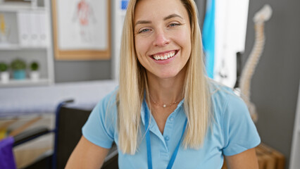 A smiling blonde woman in a blue shirt posing in a modern clinic interior, evoking healthcare...
