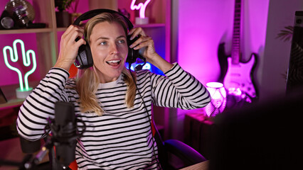 Blonde woman with headphones in neon-lit gaming room smiles engagingly, portraying leisure and technology.