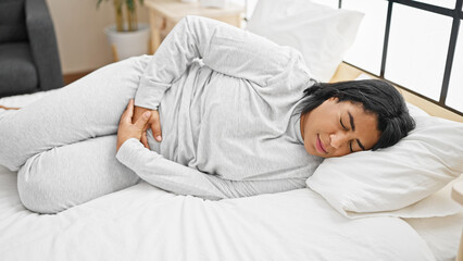 A middle-aged woman experiencing discomfort while lying in bed in a bright, modern bedroom.