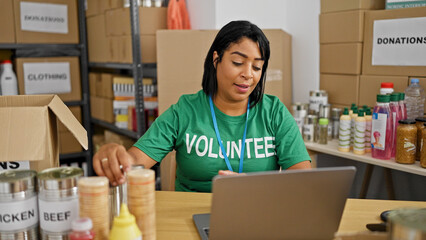 A middle-aged hispanic woman volunteers at an indoor donation center, organizing supplies and...