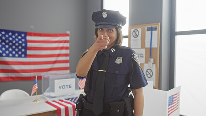 Hispanic policewoman pointing at camera in voting center with american flags