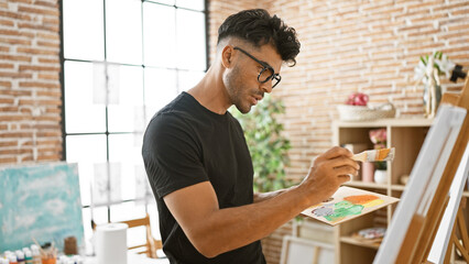 Hispanic man paints on canvas in sunlit studio, showcasing creativity and artistic talent.