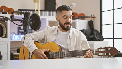 Handsome man playing guitar in a modern music studio, showcasing talent and creativity indoors.