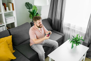 Young man spending time at home, sitting on a couch in apartment and playing arcade car video games...
