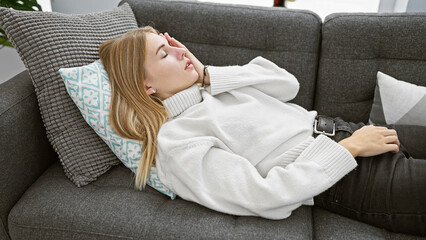 Blonde woman resting comfortably on a grey couch in a cozy living room, exuding a serene and homely ambiance.