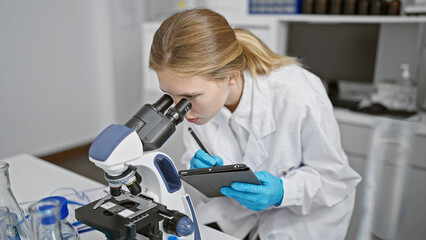 Focused woman scientist using microscope and taking notes in a laboratory setting.