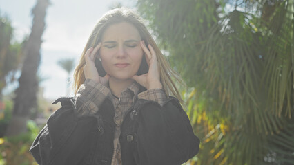 A beautiful, young caucasian woman with a headache outside in nature, touching her temples in pain.