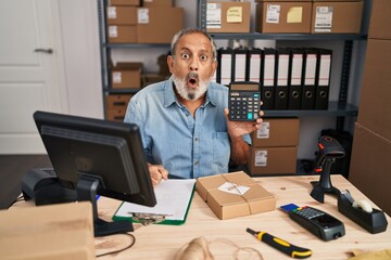 Amazed senior man with open mouth showing a face of disbelief in an office, scared as he holds calculator in surprise