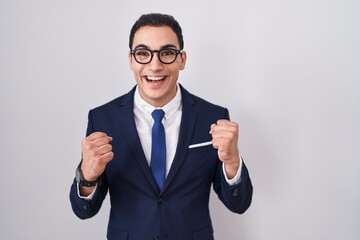 Young hispanic man wearing suit and tie celebrating surprised and amazed for success with arms raised and open eyes. winner concept.
