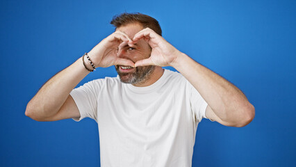 A playful handsome hispanic man with grey hair makes heart shape with hands against a vibrant blue...