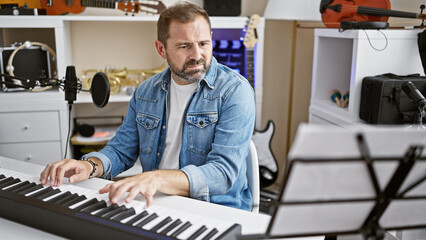 Mature handsome hispanic man playing electronic piano in a modern music studio setup.