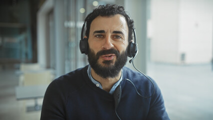 Naklejka premium Handsome bearded man wearing headphones smiling in a bright modern office setting.