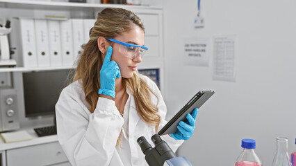 Serious and beautiful blonde woman scientist, deep in thought at lab, young pro working on touchpad...