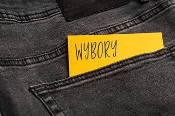  Yellow card with a handwritten inscription "Wybory", inserted into the pocket of gray pants jeasnow (selective focus), translation: elections