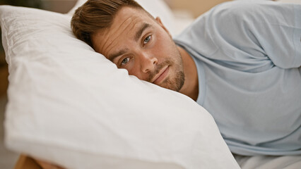 Handsome young hispanic man with beard lying in bedroom looking tired or thoughtful.