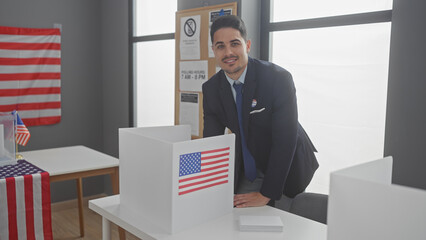 A handsome hispanic man wearing a suit smiles confidently inside a voting center adorned with...