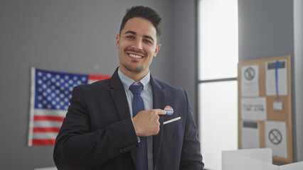 Handsome young hispanic man with beard, wearing suit, pointing at 'i voted' sticker with american...