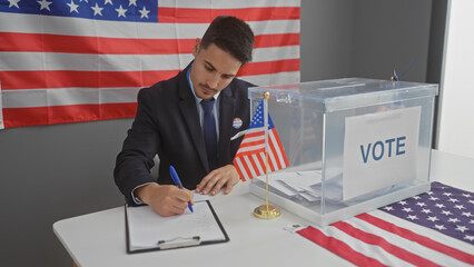 Young hispanic man voting at an indoor electoral table with american flag backdrop.