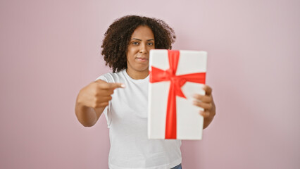 Black woman with curly hair presenting a gift with a red ribbon on a pink background