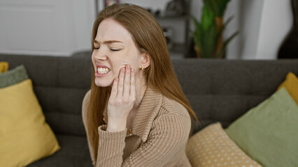 A young woman expressing pain while touching her cheek in a cozy living room setting.