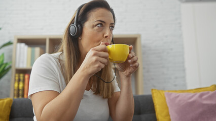 A thoughtful hispanic woman enjoys coffee and music in her modern living room.