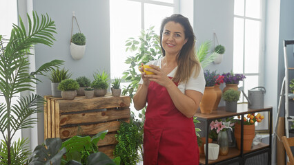 Hispanic woman smiling in a green-filled indoor setting wearing an apron and holding a yellow cup