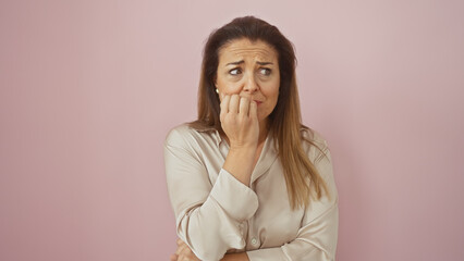 An anxious hispanic woman in a beige blouse poses against a solid pink background, appearing...