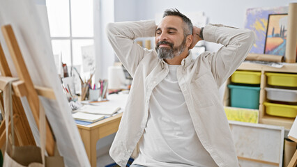 Relaxed bearded senior man with grey hair enjoying a creative break in a bright art studio.