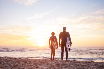 The sun sets over ocean waves as two surfers stand and watch