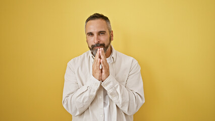 Mature bearded hispanic man with grey hair posing against a yellow wall, conveying thoughtfulness.