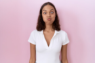 Fototapeta premium Young hispanic woman wearing casual white t shirt puffing cheeks with funny face. mouth inflated with air, crazy expression.