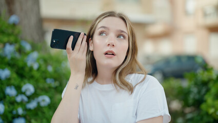 Young caucasian woman listening audio message by the smartphone with serious expression at park