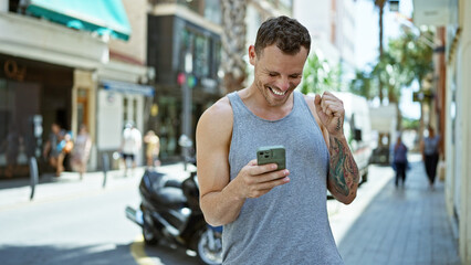 Hispanic man smiling and using smartphone on a sunny urban street, radiating a relaxed and happy...