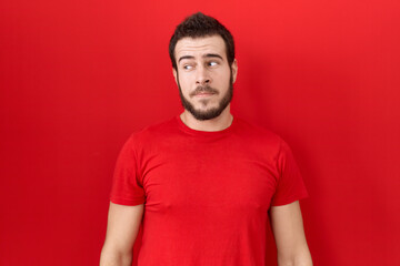 Young hispanic man wearing casual red t shirt smiling looking to the side and staring away thinking.
