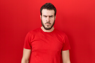 Obraz premium Young hispanic man wearing casual red t shirt skeptic and nervous, frowning upset because of problem. negative person.