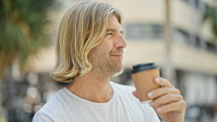 Handsome man with long blond hair holding coffee on a sunny urban street